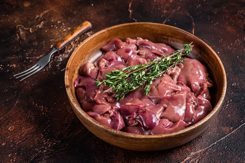 Raw chicken liver offals in a wooden plate. Dark background. Top view.